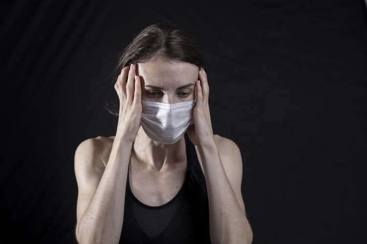 Is COVID-19 Making Your Tinnitus Worse? Woman wearing mask and holding hands up to her ears.