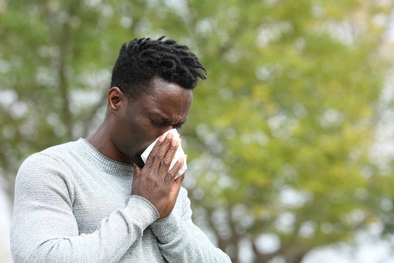 Man with allergies blowing his nose in an outdoor park.