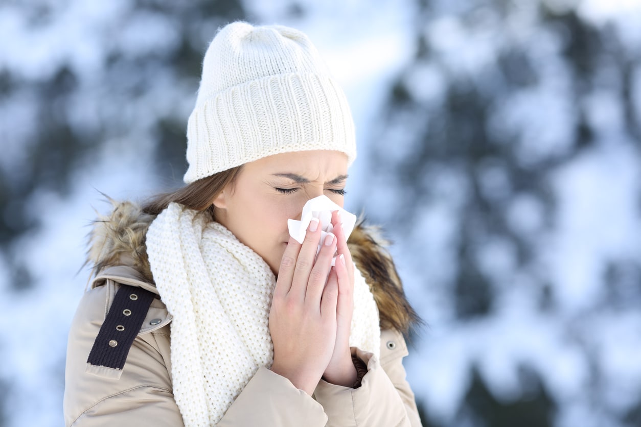Woman in the snow blowing her nose.
