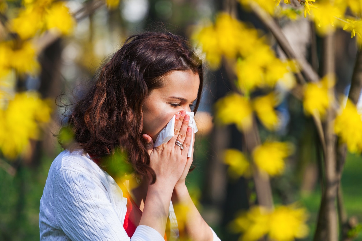 Woman blowing her nose amidst a bunch of flowers.