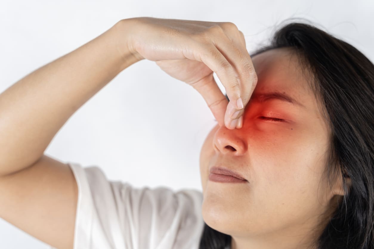 Woman with sinus pressure holding her red nose.