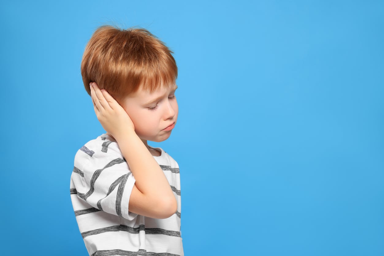 Young boy holding his ear on a blue background.