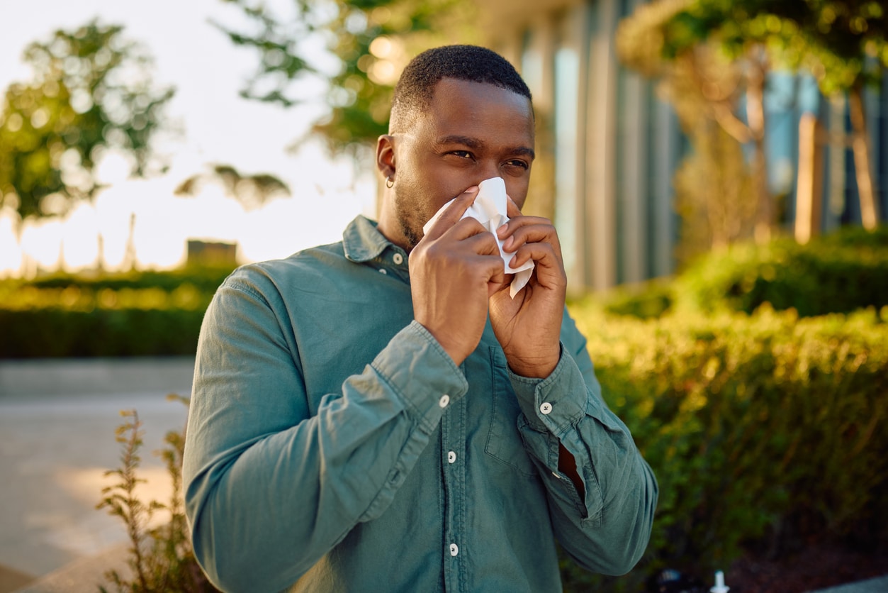 Man blowing his nose with a tissue outdoor.