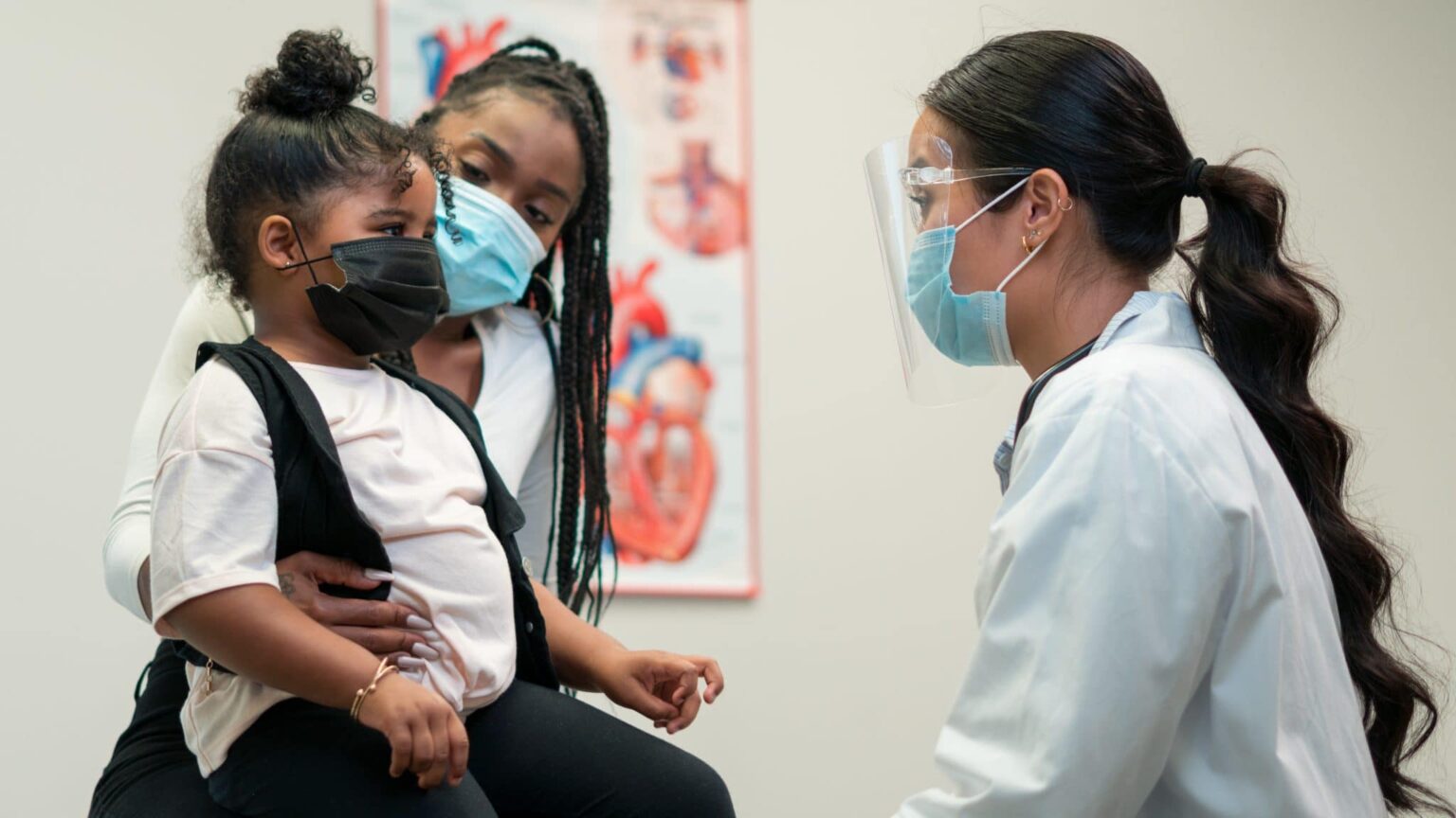 Mom and daughter visiting with their doctor, masks on.