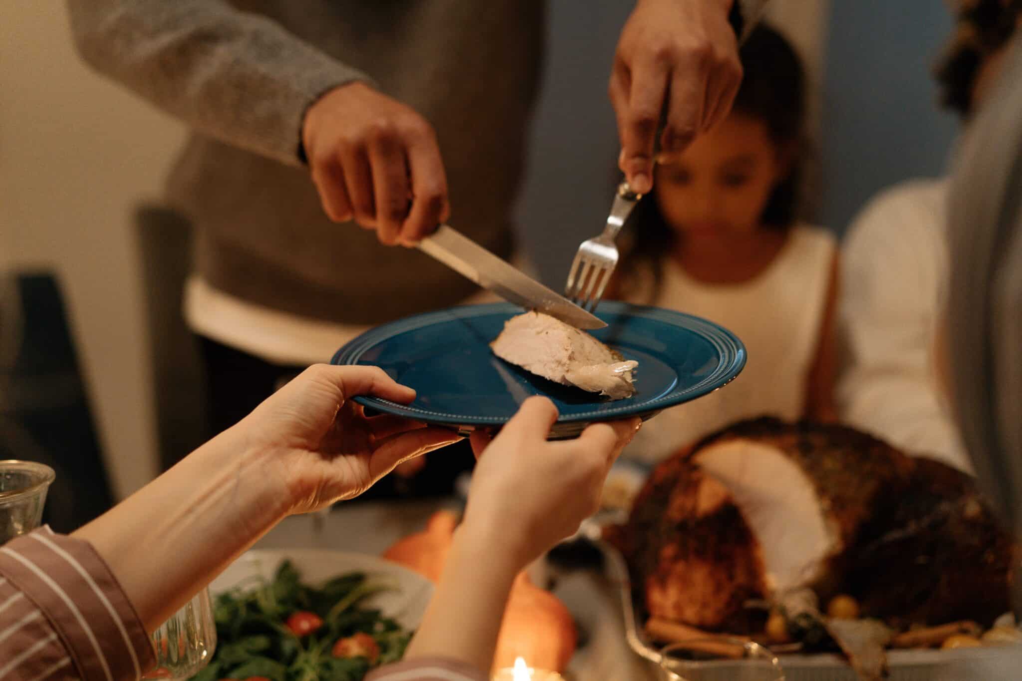 A family getting ready to eat thanksgiving together, cutting turkey on a plate.