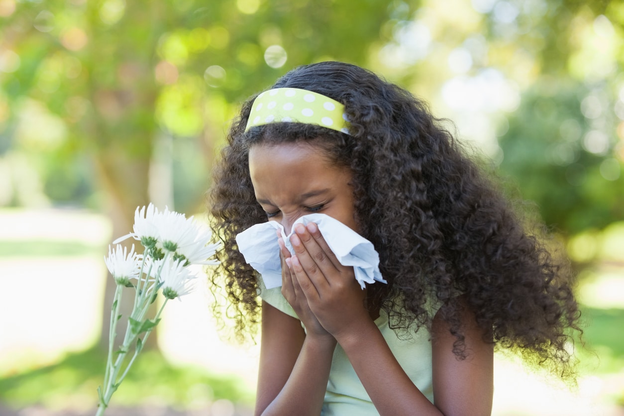 Young girl sitting by flower and blowing her nose in the park