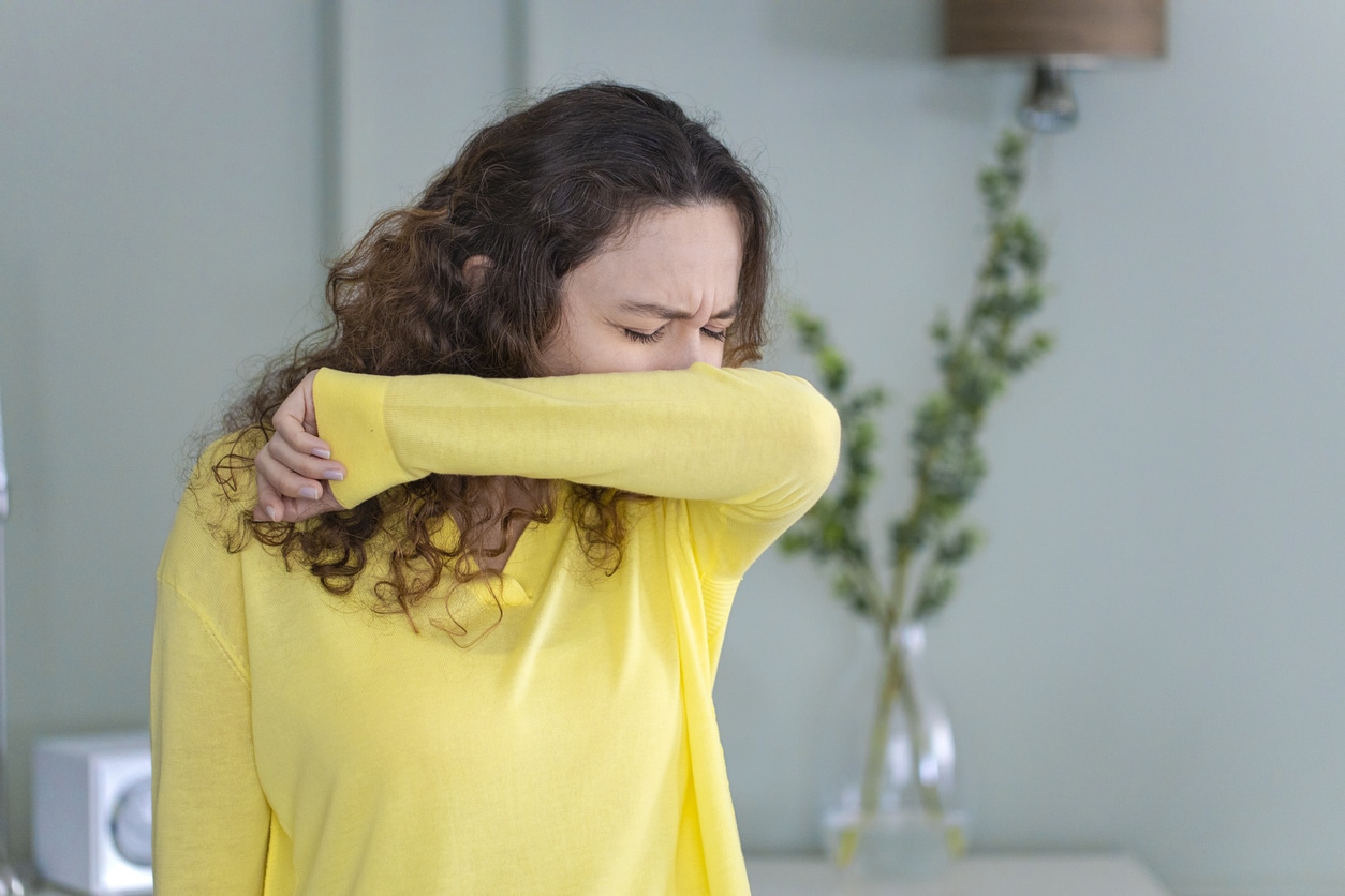 Woman sneezing into her elbow at home